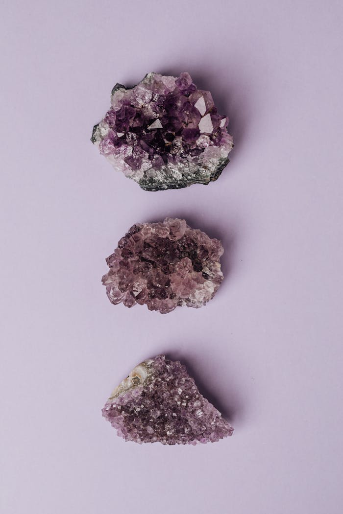 Three amethyst crystal clusters arranged on a pastel purple background, showcasing their natural beauty.